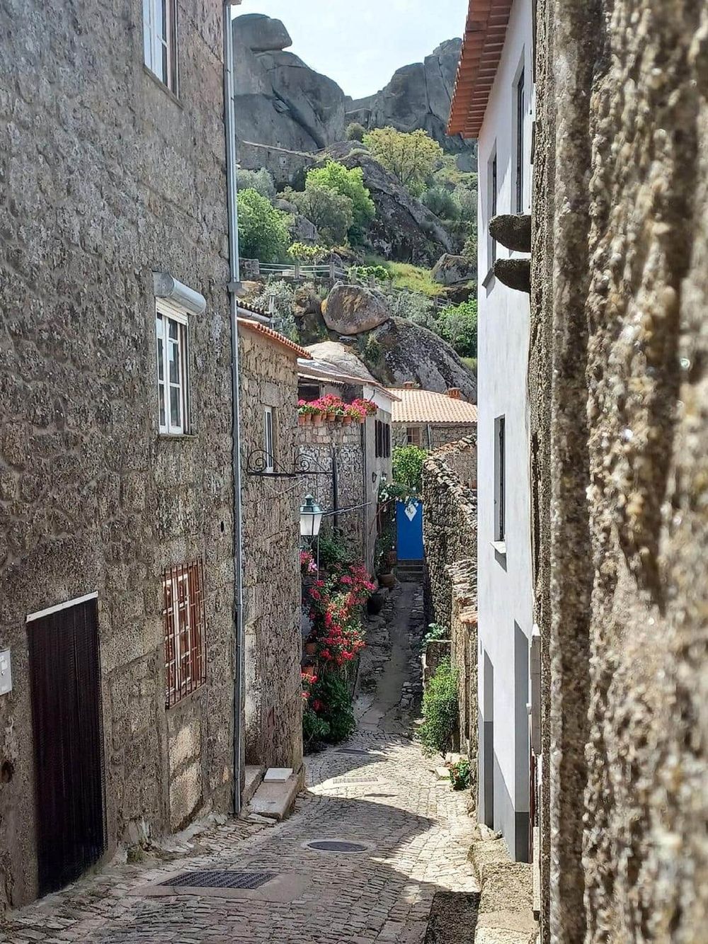 Charming narrow cobblestone street in an old European village with rocky hillside in the background.