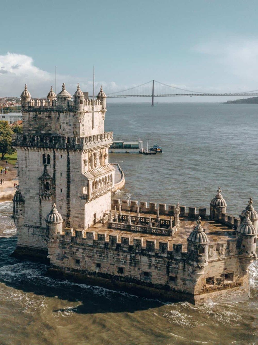 Medieval castle by river with Lisbon bridge in background, Portugal.