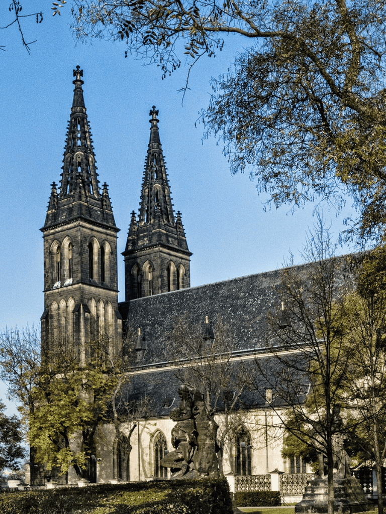 Ancient Gothic church with twin spires, surrounded by trees, under a clear blue sky.