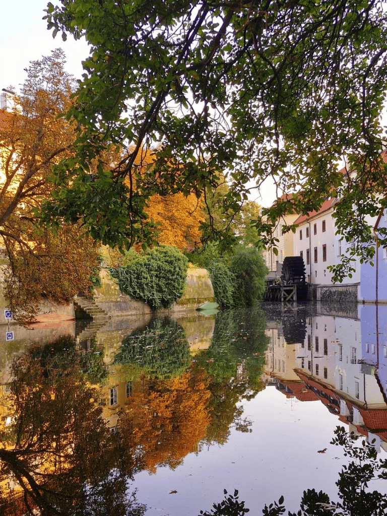 Tranquil canal scene with autumn trees, historic buildings, and reflections, perfect for exploring scenic routes.