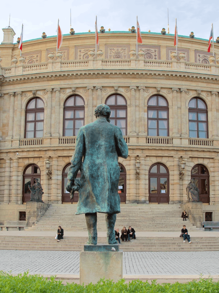 Statue of a man in front of historic building, government or cultural landmark, urban scene, public art.