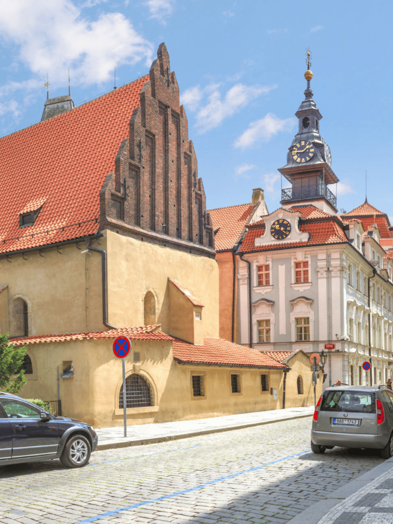 Historic European church with clock tower, cobblestone street, and cars in Czech city.