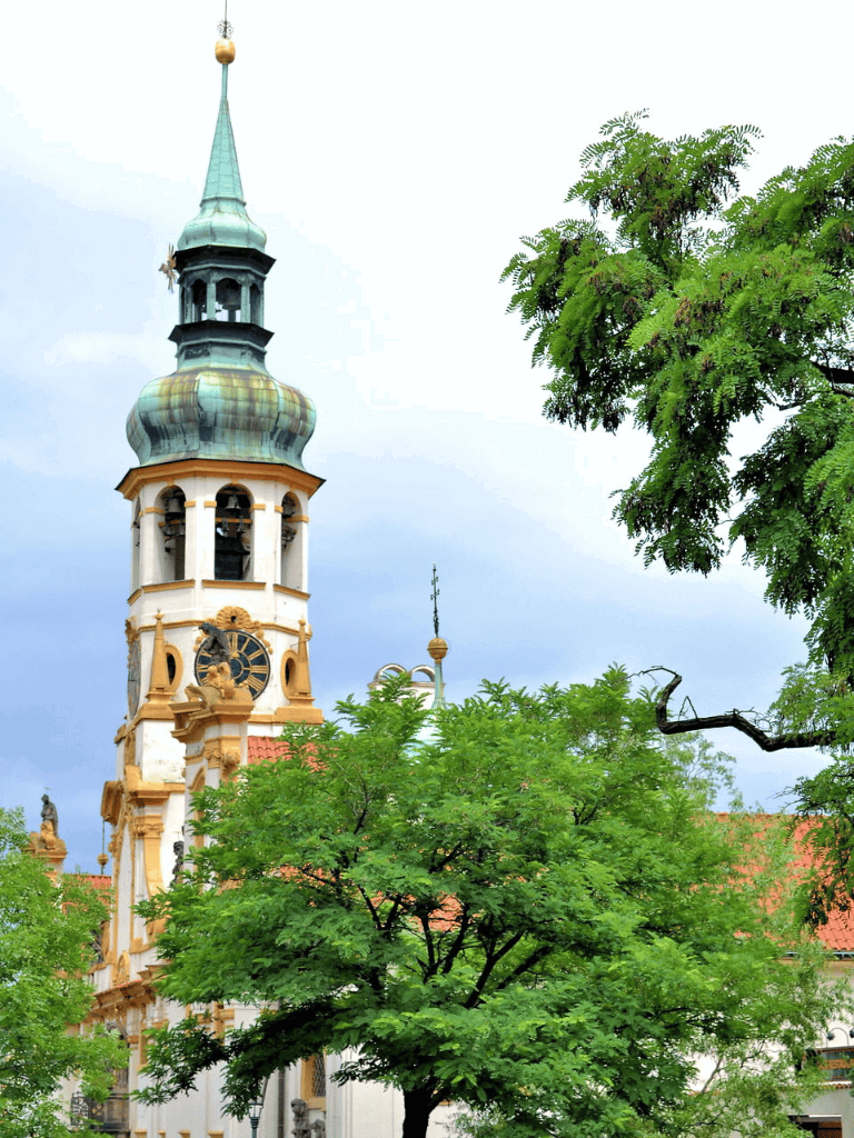 Historic church steeple and clock tower surrounded by lush green trees in a scenic European town.