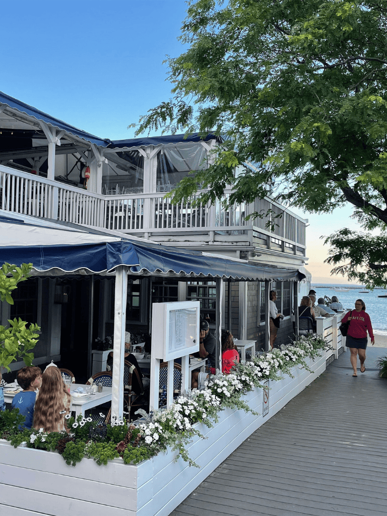 Outside dining waterfront restaurant with scenic ocean view and lush greenery.