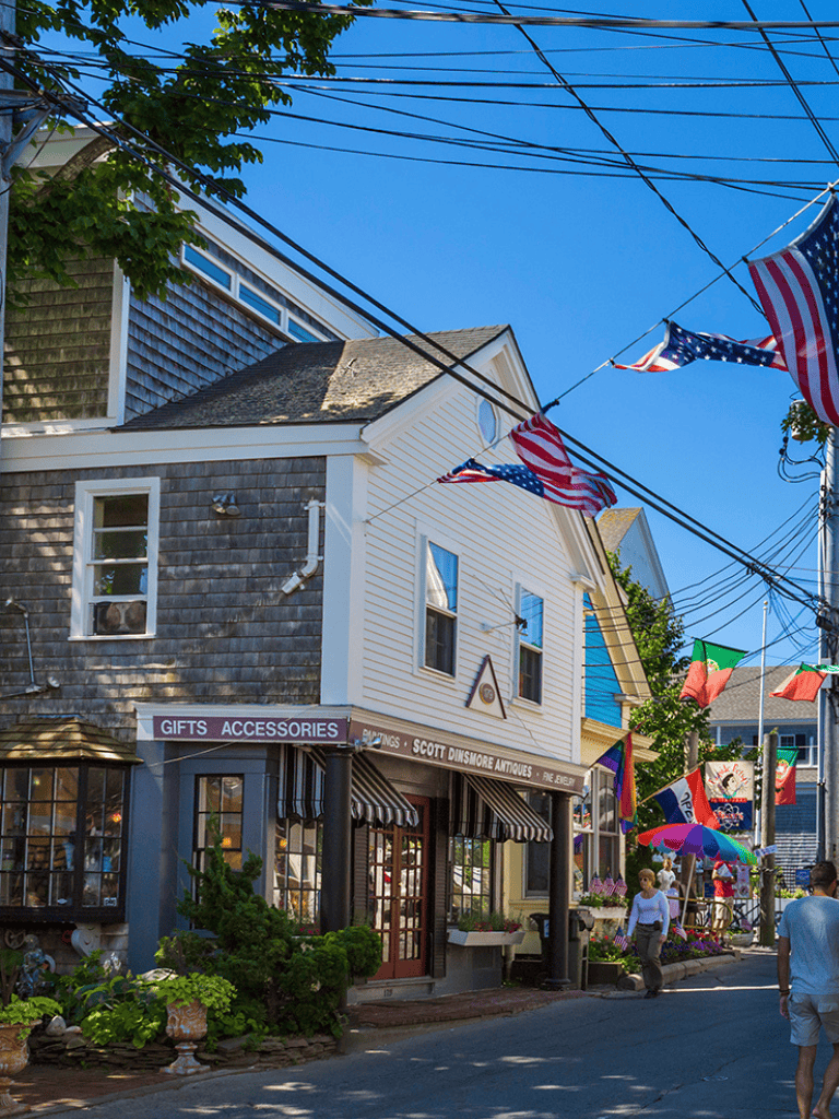 Colorful street scene in seaside town with shops, flags, and pedestrians, showcasing vibrant local shopping and community life.