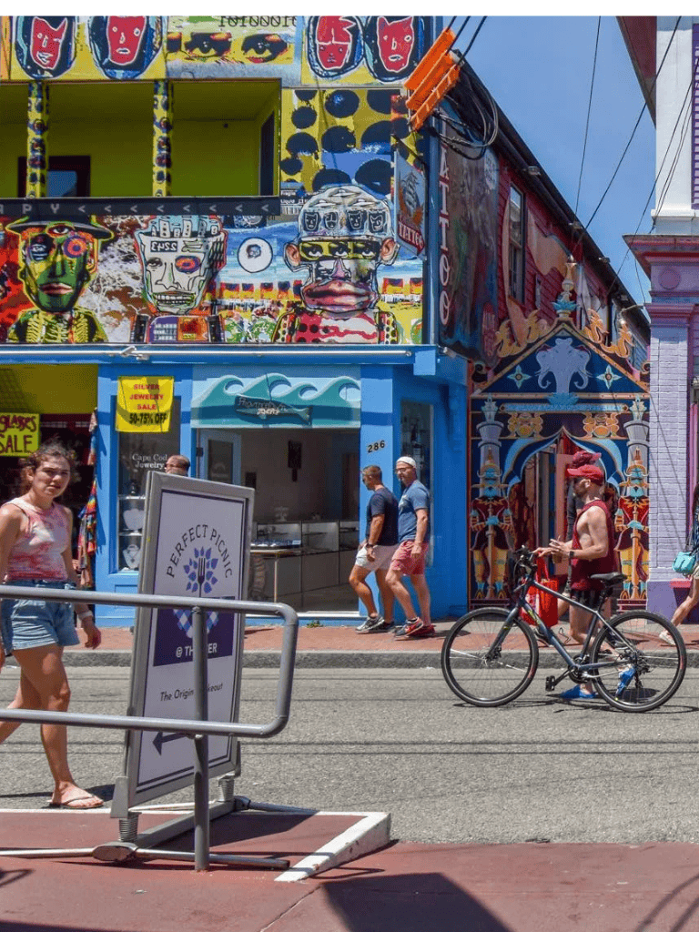 Vibrant colorful street art murals in a lively urban shopping district with pedestrians and cyclists.