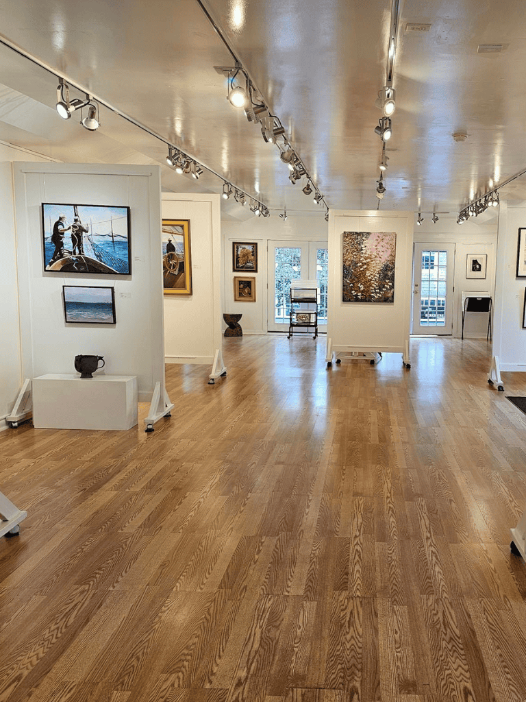 Colorful art gallery showcasing modern paintings and sculptures with natural light and wooden flooring.