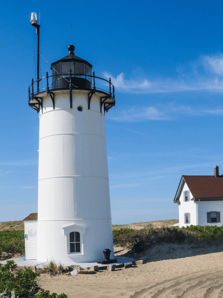 Lighthouse on sandy beach under blue sky, coastal navigation, scenic lighthouse view, QuestForDirections.
