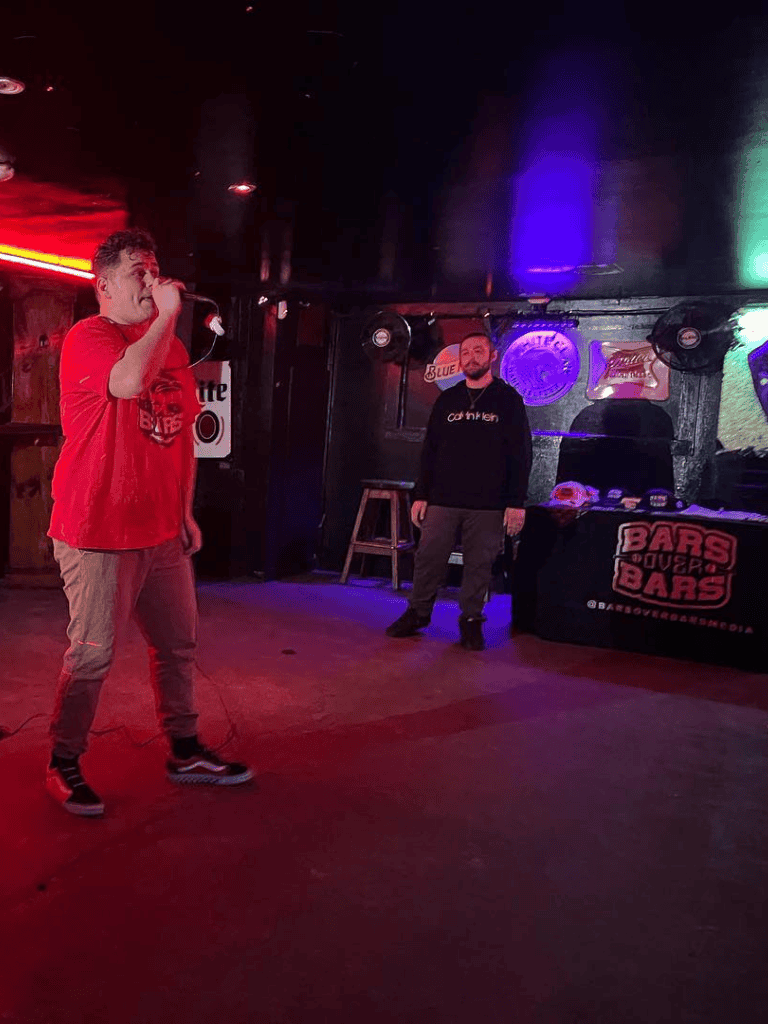 Young man performing karaoke at a lively bar event, night setting with colorful lighting.