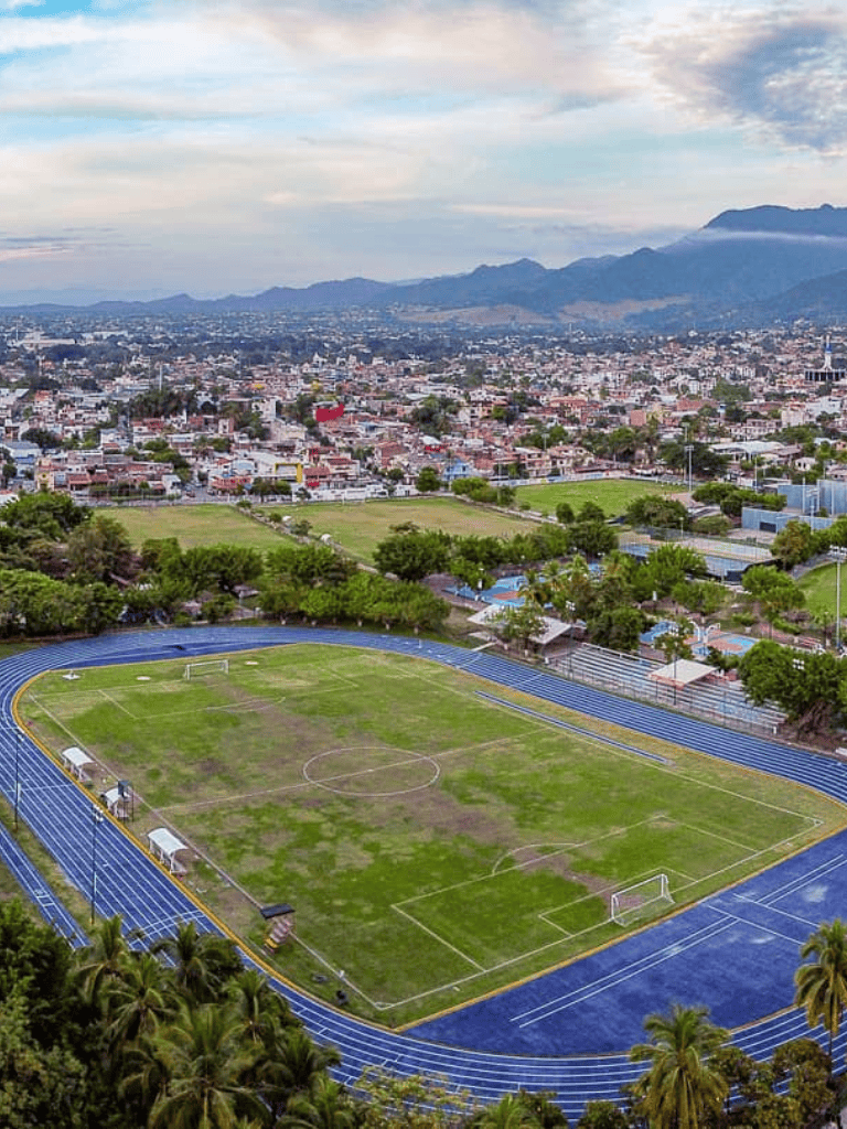 Aerial view of a city with sports fields and surrounding mountains, showcasing urban development and outdoor recreation spaces.