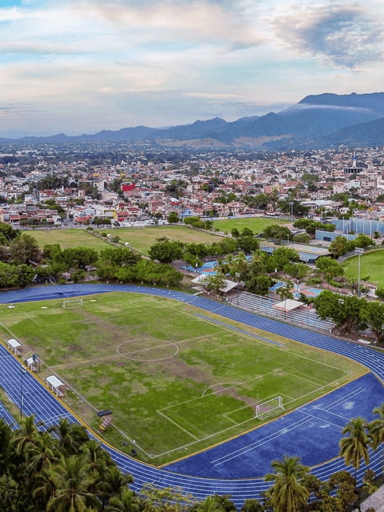 Aerial view of a sports field and cityscape with mountains in the background during daytime.