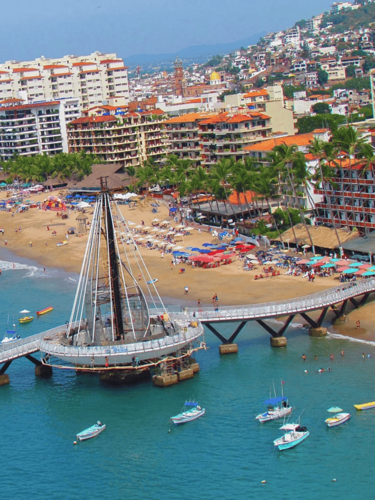 Colorful beachfront with pier, boats, high-rise hotels, and vibrant cityscape in Acapulco, Mexico.
