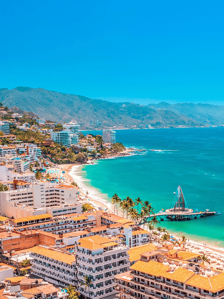 Aerial view of Cancun coast with clear turquoise waters, white sandy beaches, and high-rise hotels under a bright blue sky.