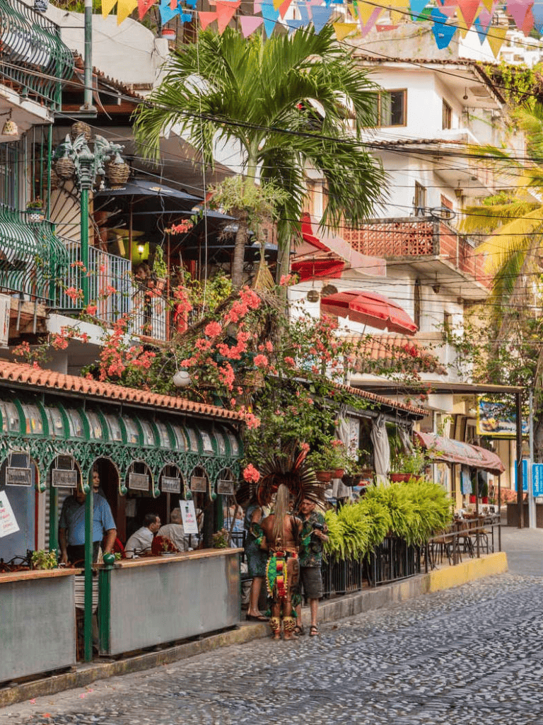Colorful street scene with cafes, palm trees, and vibrant decorations in a lively urban area.