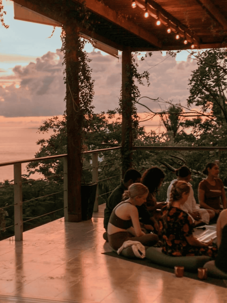 Sunset yoga class overlooking sunset at tropical forest retreat, people practicing yoga and meditation, peaceful nature escape.