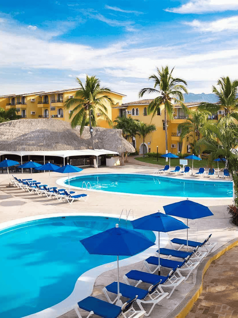 1. Beautiful poolside at resort with blue umbrellas, palm trees, and yellow buildings in the background.