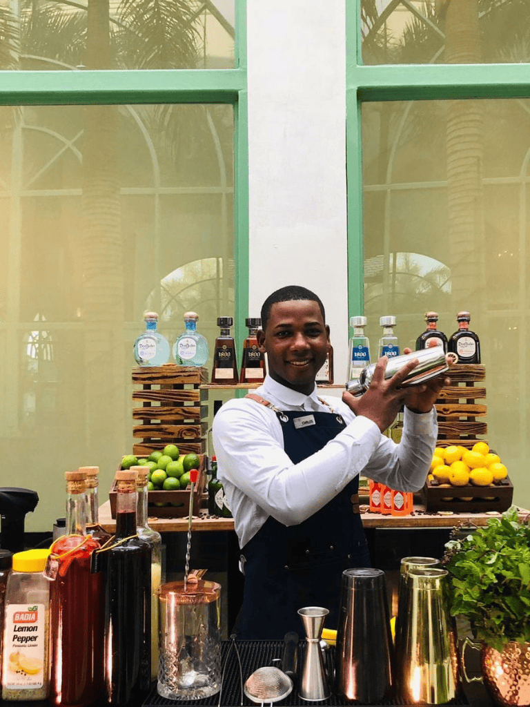 Bright bartender preparing cocktails at a colorful bar with fresh ingredients and premium spirits.