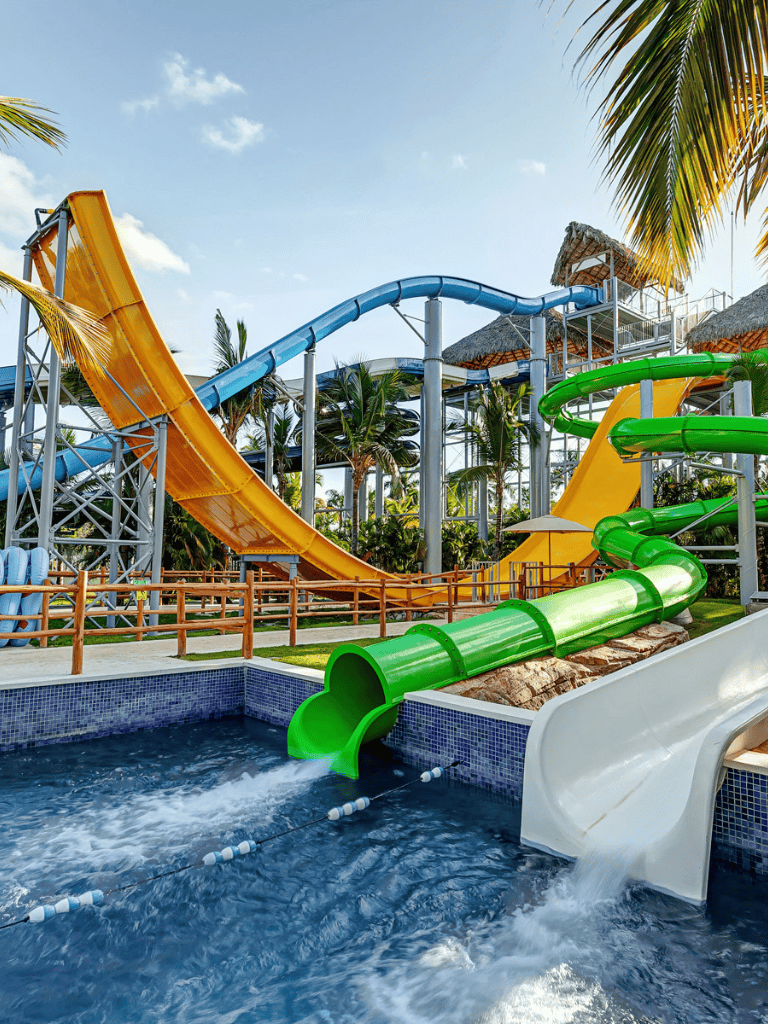Colorful water slides at a tropical waterpark under a blue sky with palm trees.