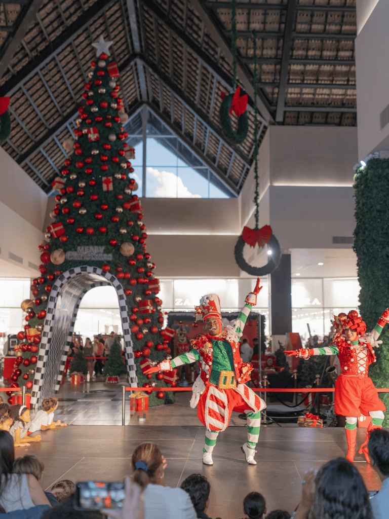 Festive Christmas tree inside mall with holiday decorations and performers entertaining children during holiday season.