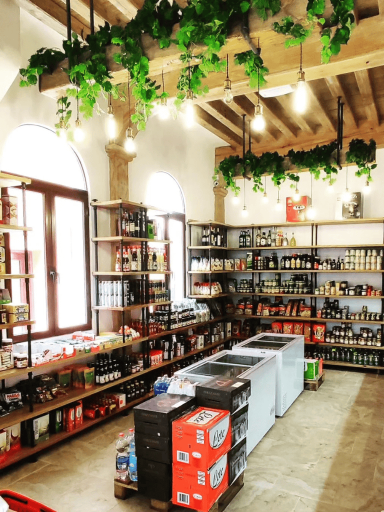 Bright interior of a gourmet grocery store with wooden shelves and hanging green plants.