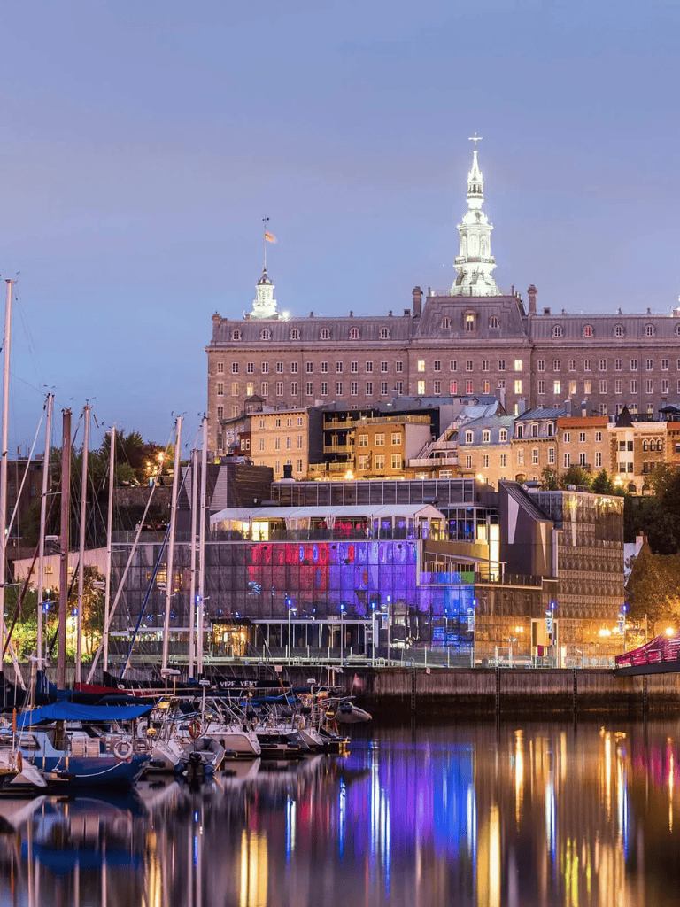 Aerial view of a historic waterfront cityscape with a prominent castle-like building illuminated at dusk.