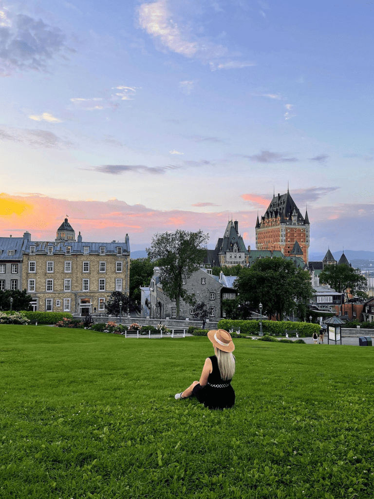 Chateau Frontenac in Quebec City at sunset with woman sitting on grass, scenic travel destination, historic architecture, tourism.