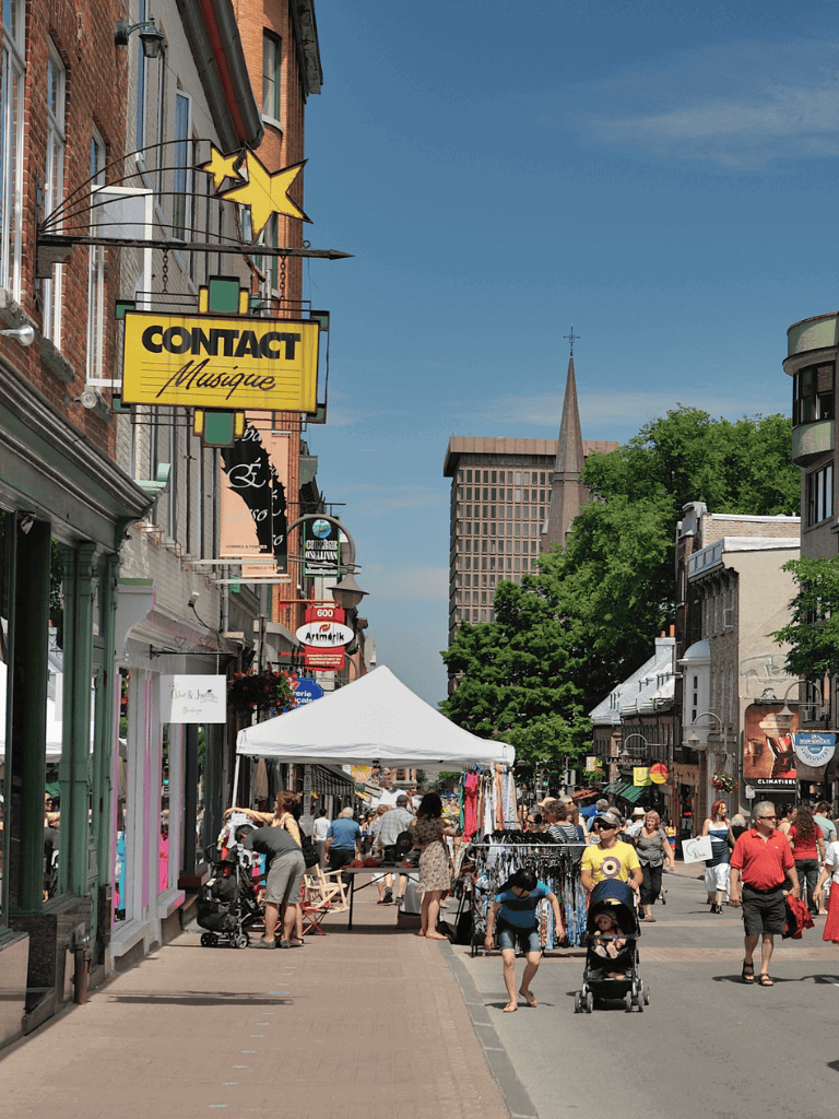 Vibrant downtown street with shops, shoppers, and outdoor market stalls, ideal for exploring local businesses and culture.