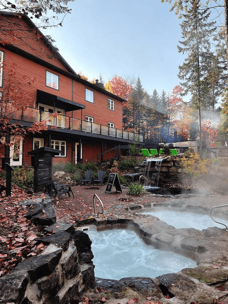 Outdoor hot springs with a red lodge, surrounded by autumn trees, offering a relaxing retreat.
