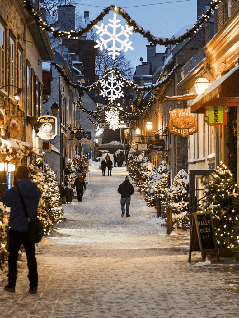 Festive winter street decorated with Christmas lights, snow-covered trees, and holiday ornaments.