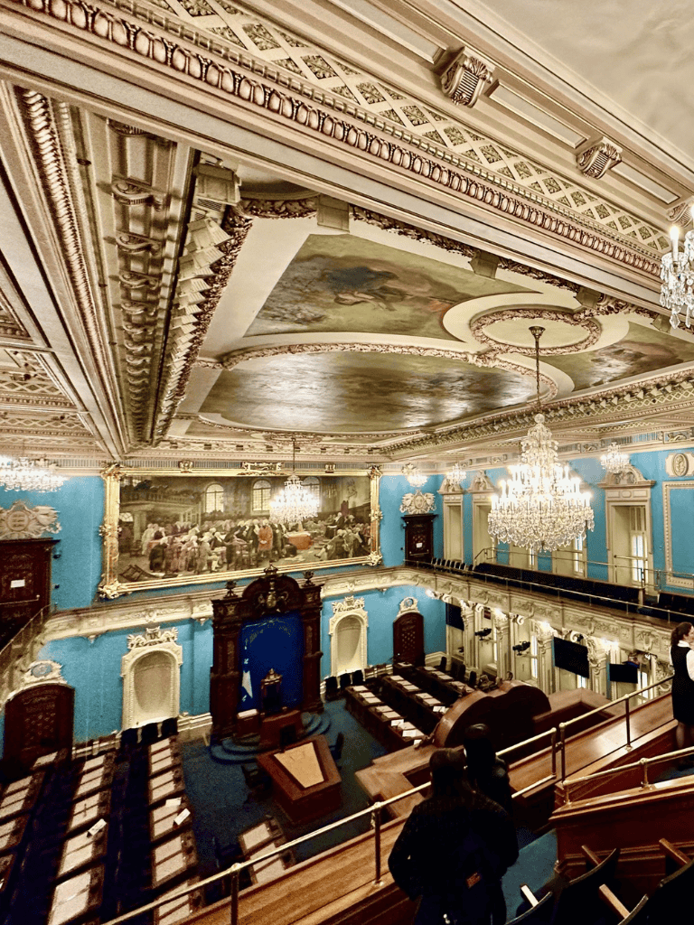 Opulent historic meeting room with ornate ceilings and chandeliers, elegant blue walls, and classical murals.