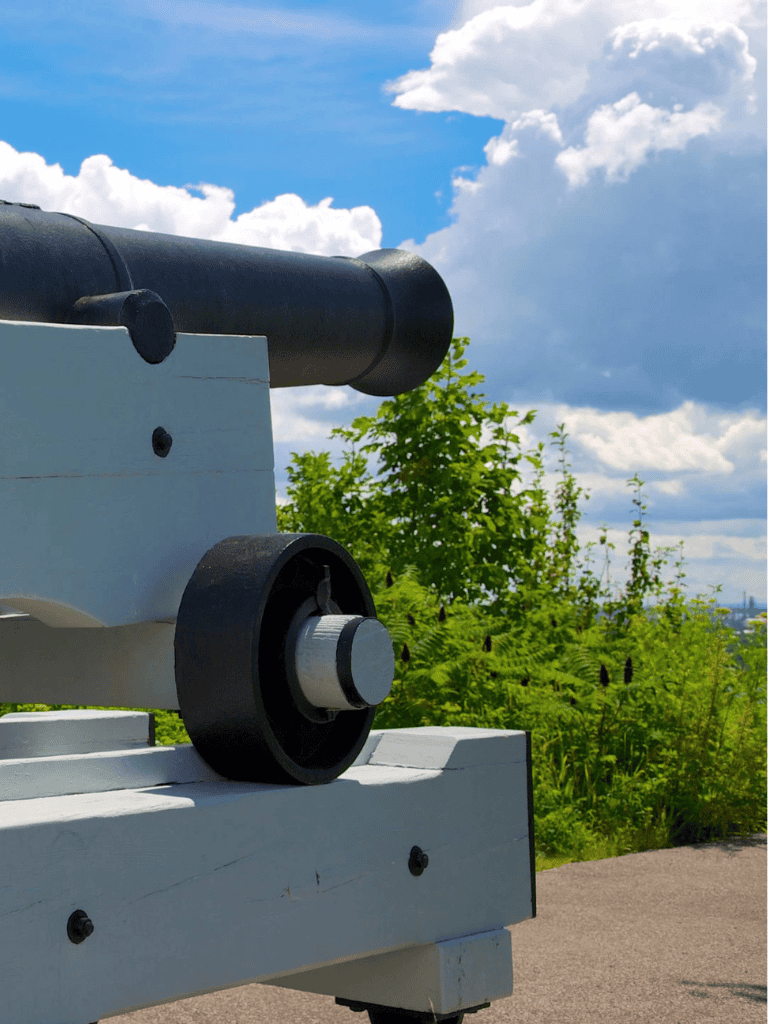 Cannon on a mountain deck with a lush green landscape and partly cloudy sky.