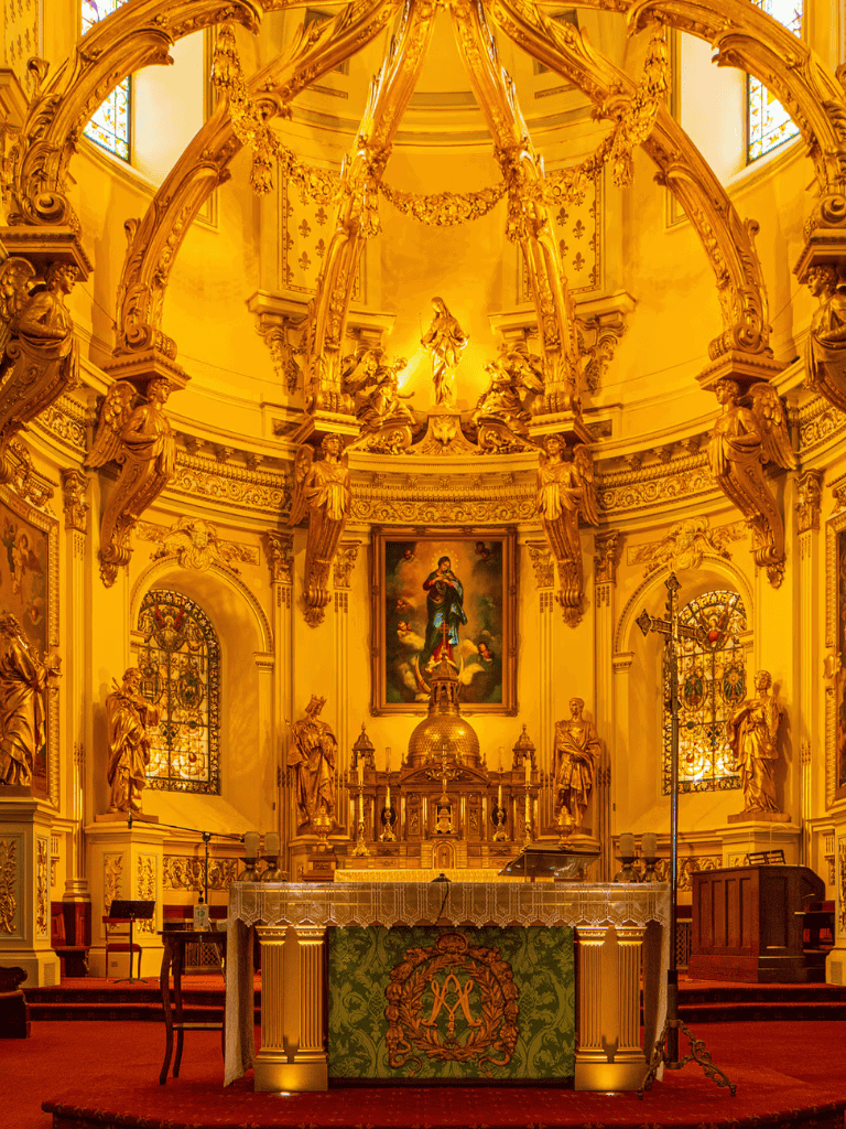Intricate gold altar with religious statues and artwork inside a luminous church.