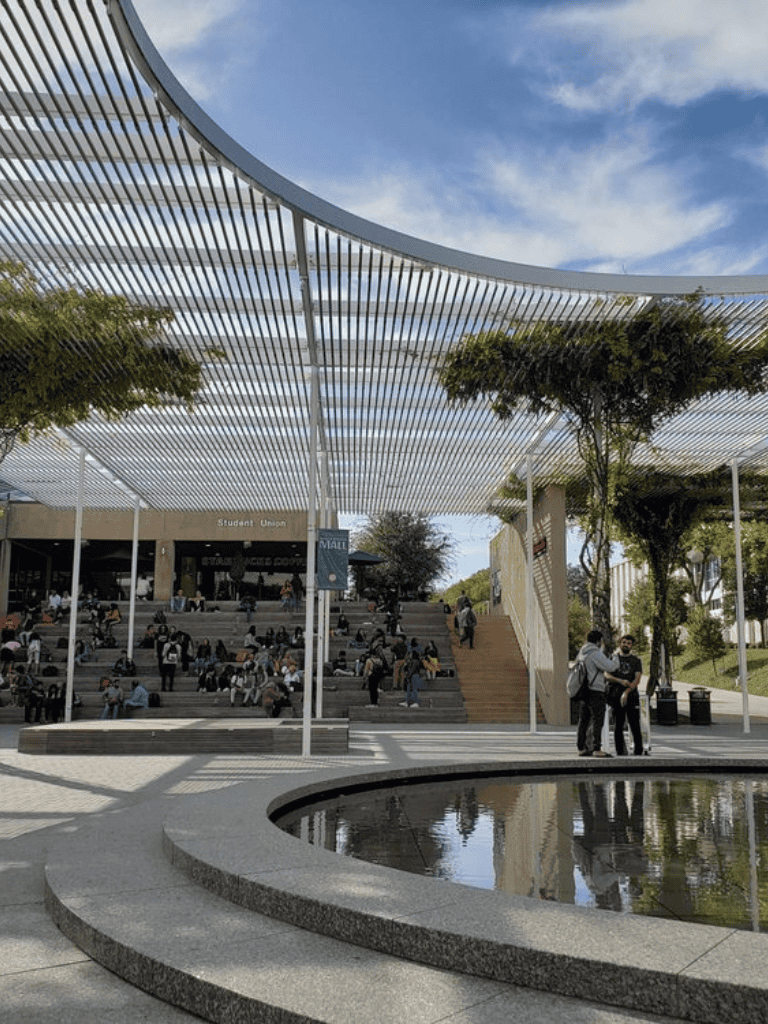 Modern university student union building with outdoor seating and architectural shading structure, vibrant campus scene.