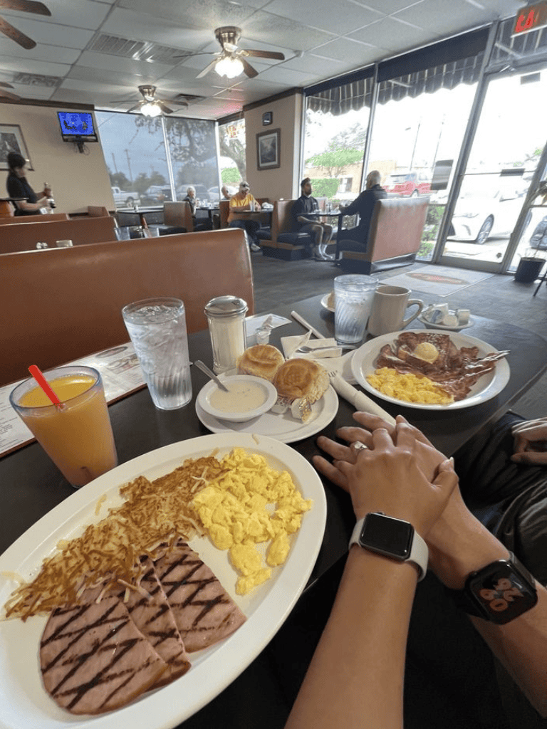 Breakfast meal with scrambled eggs, ham, pancakes, and beverages at a cozy diner restaurant.