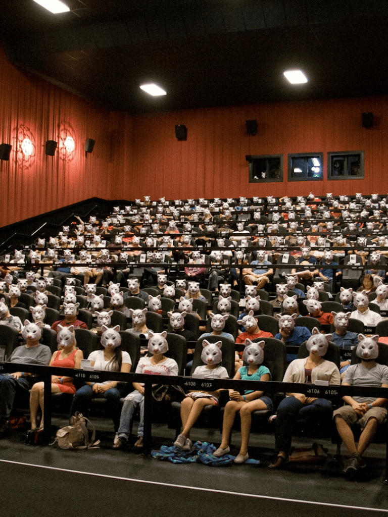 People wearing pig masks sitting in a theater auditorium, attending a film screening or event.