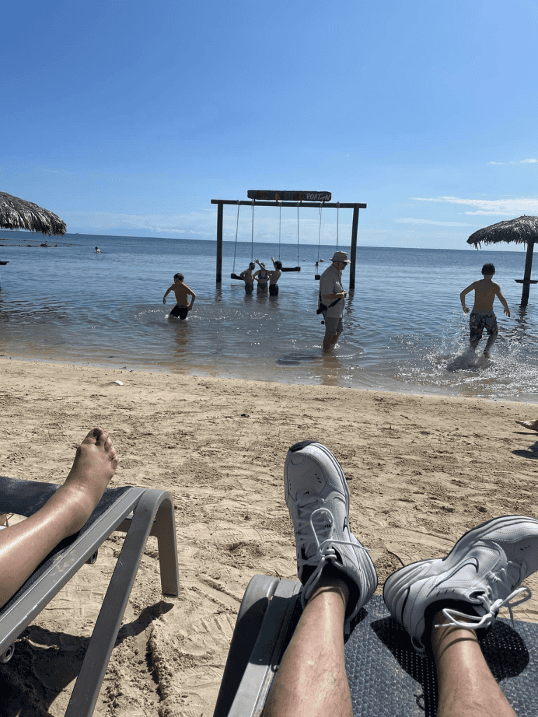 Relaxing beach scene with swimming children and a person lounging on beach chair, scenic ocean view, tropical getaway.