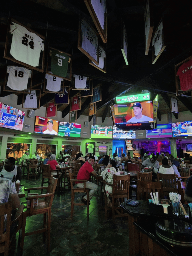 Bright sports bar with multiple TVs showing baseball games and hanging jerseys above.
