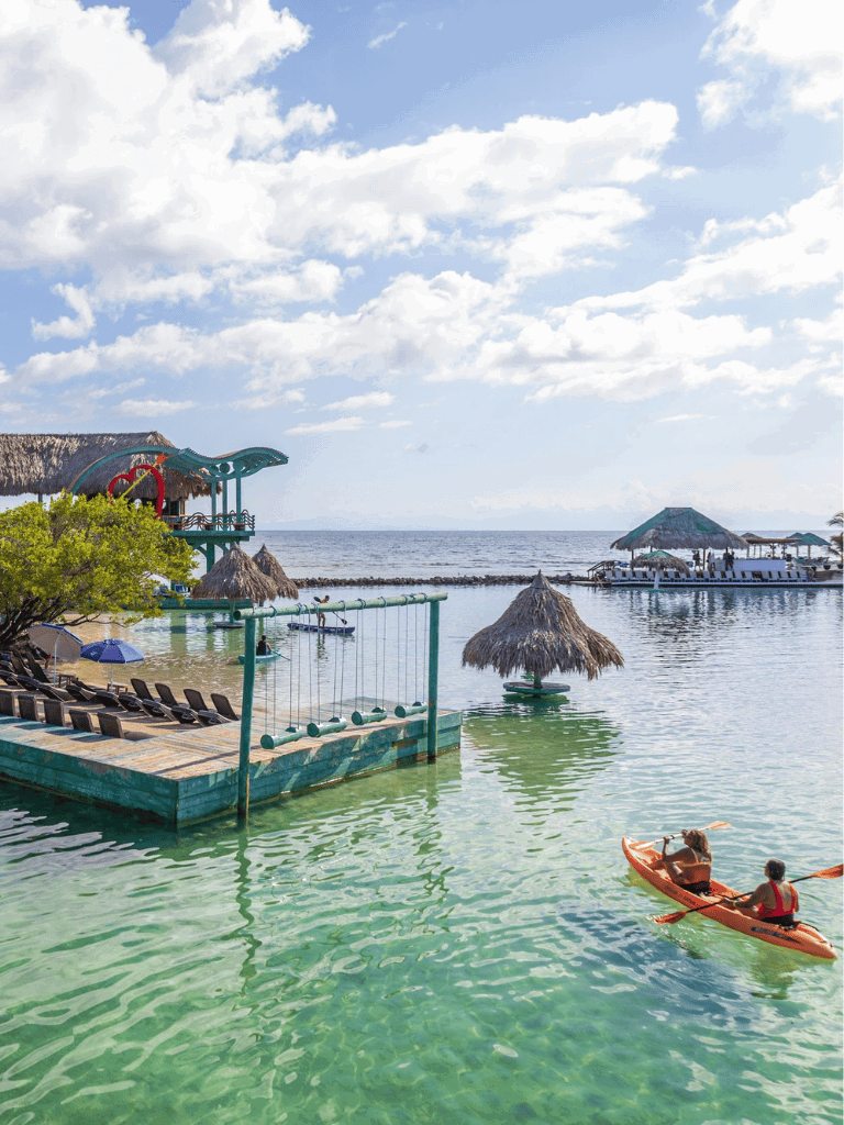 Colorful beach resort with kayaks, thatched umbrellas, and water slides on a sunny day at the seaside.