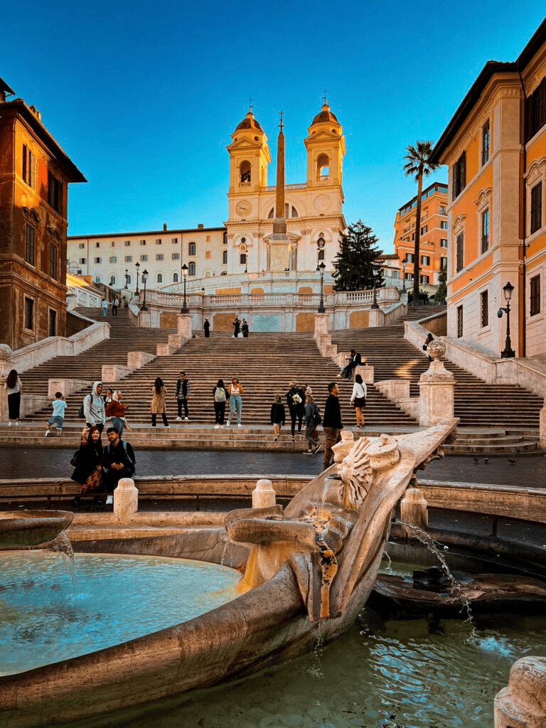 Ancient Roman-style staircase and fountain in Rome, Italy, with visitors enjoying the historic site.