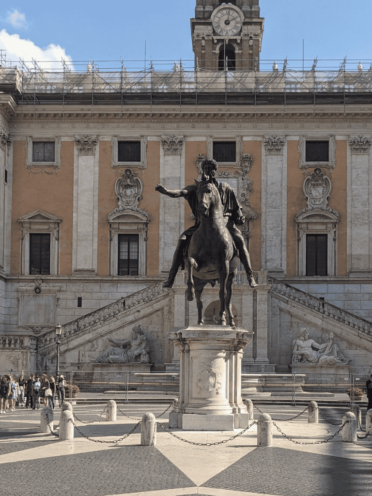 Bronze equestrian statue in front of historic building with clock tower, Rome Italy, at sunset.