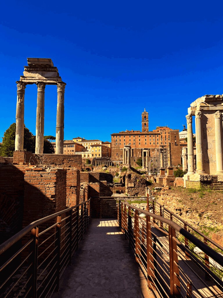 Ancient Roman ruins in Rome with historic columns and cityscape under clear blue sky.