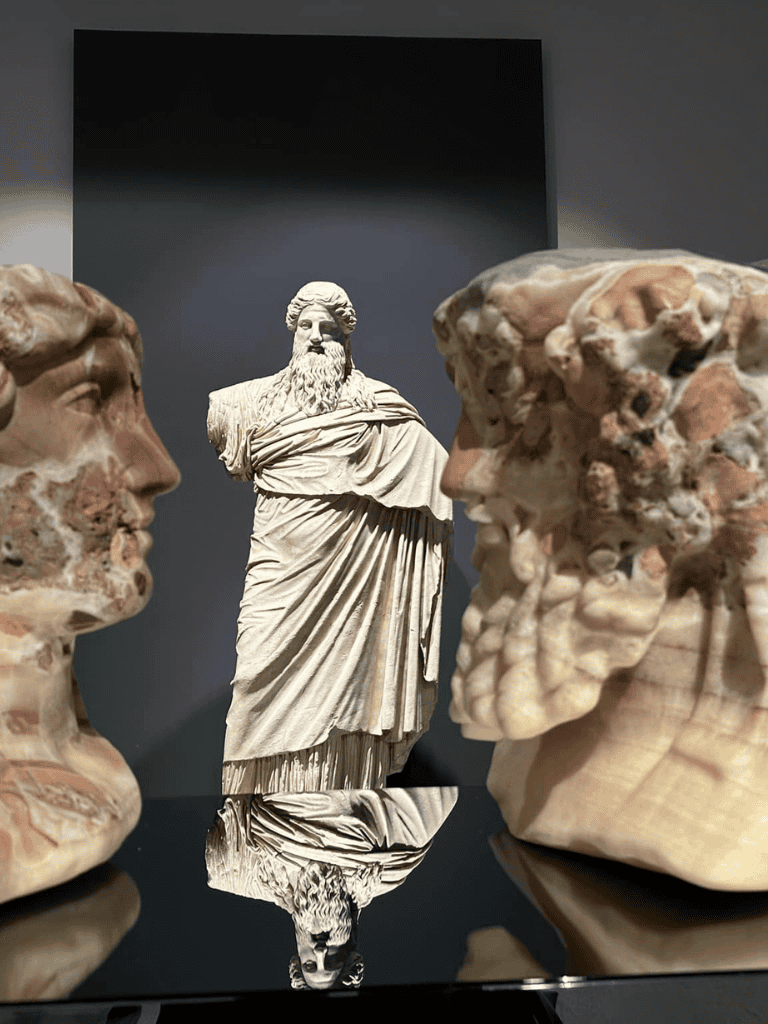 Ancient Greek sculptures and busts displayed in a museum exhibit.