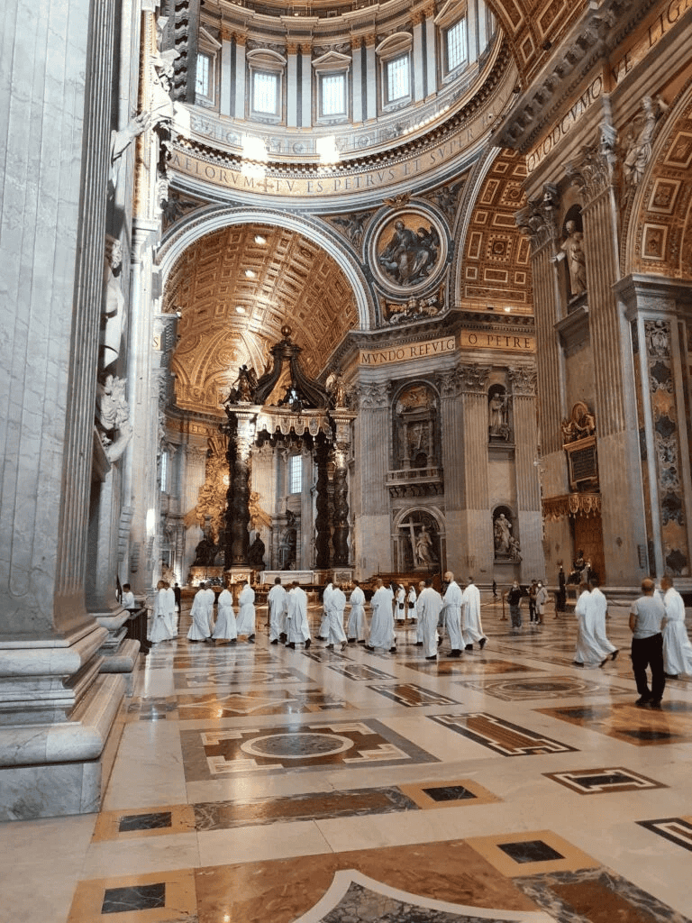 Lavish baroque cathedral interior with clergy, detailed architecture, and ornate decorations.