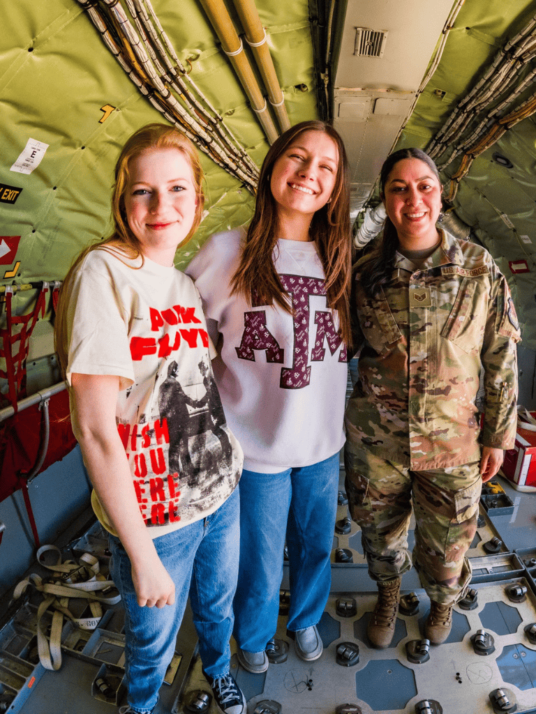 Female soldiers and students smiling inside military aircraft.