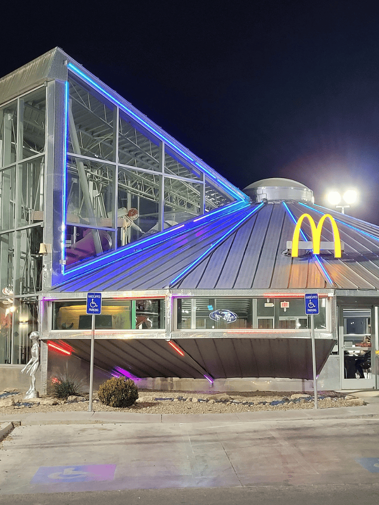 Night view of a modern McDonald's restaurant with neon lighting, accessible parking, and drive-thru, highlighting iconic fast-food branding.