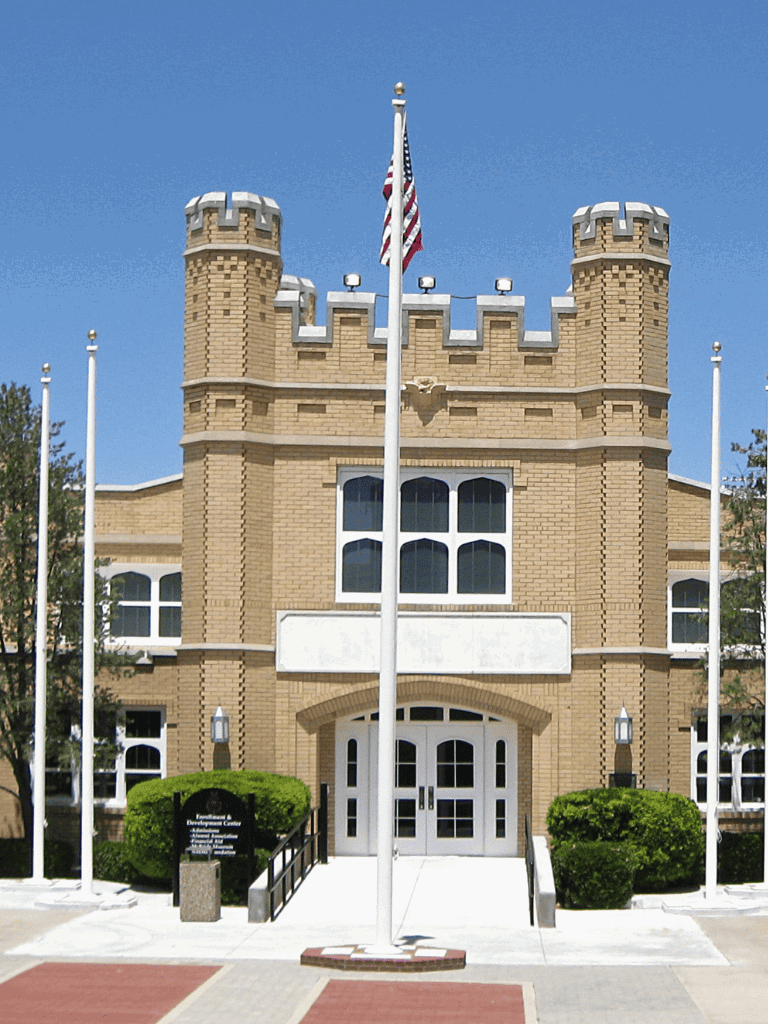 Historic castle-style building with American flag in front, bright blue sky.