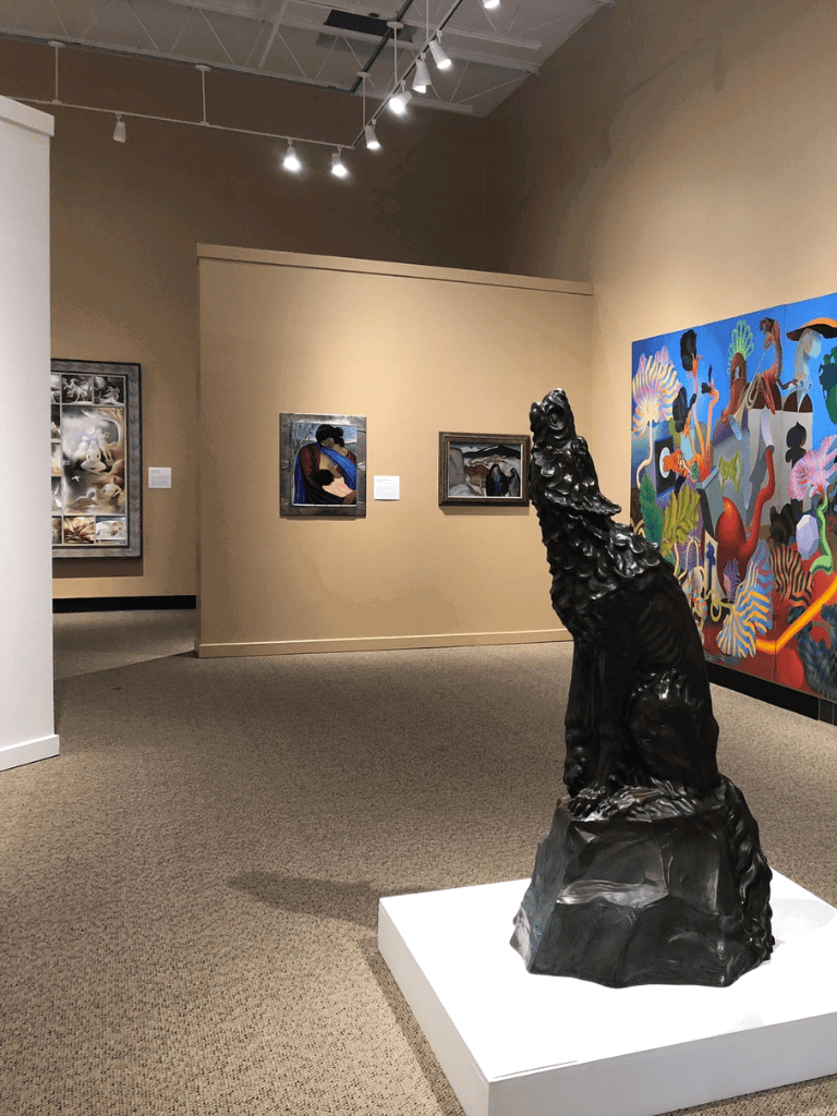 Intriguing bronze lion sculpture in an art gallery with colorful paintings in the background.