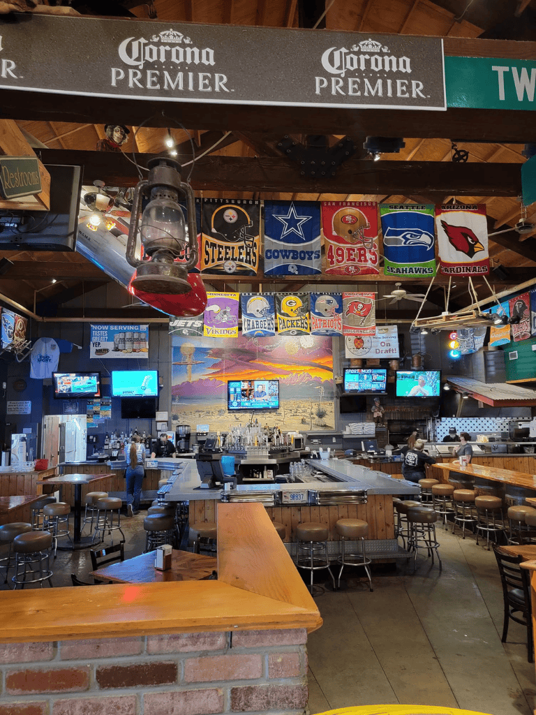 Colorful sports flags hanging in a lively sports bar with multiple TV screens and a bar counter.