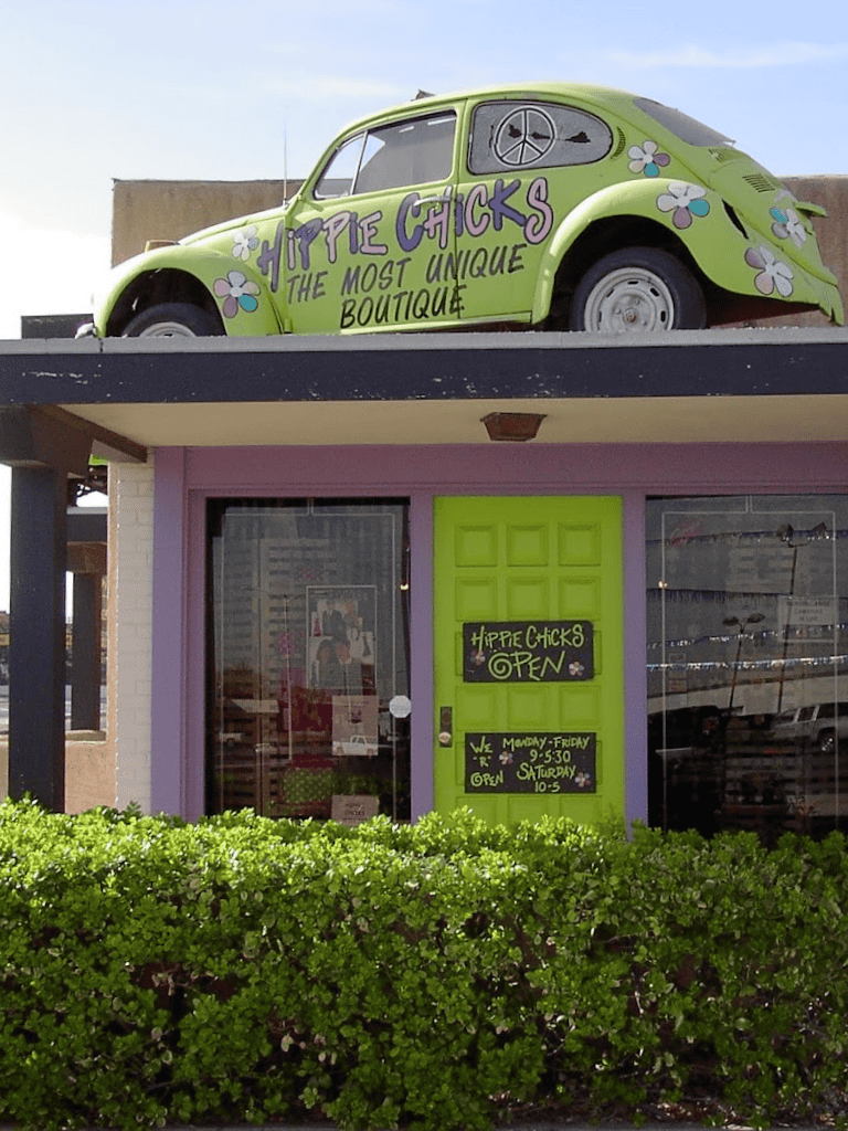 Vibrant green boutique storefront with purple accents, featuring a vintage Volkswagen car on the roof.