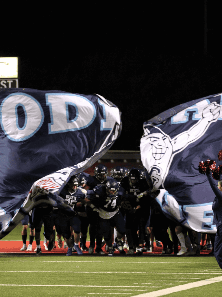 Rockets football team entering the field with large team flags at night.